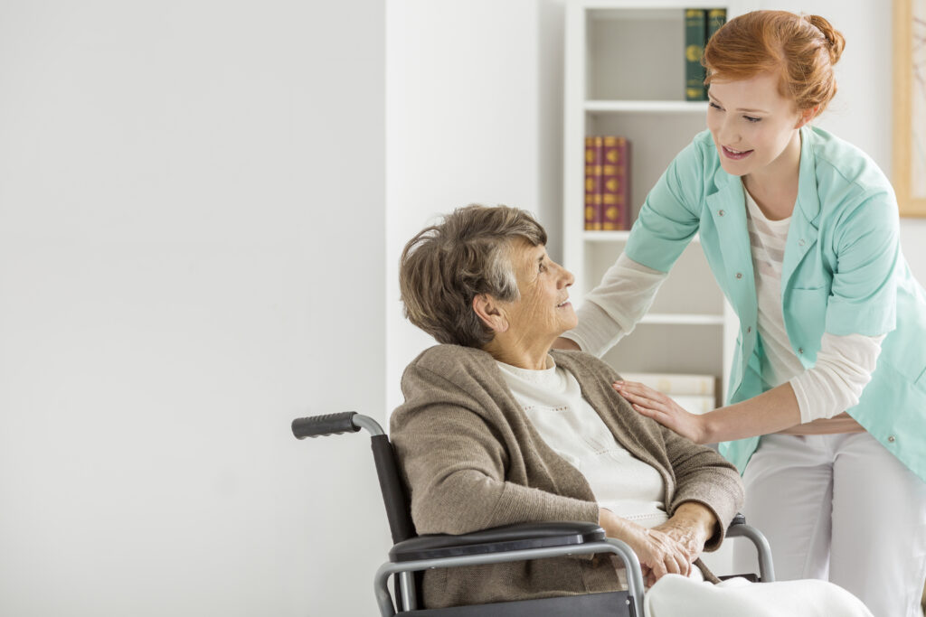 carer administering help to elderly patient in wheelchair